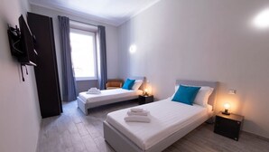 A hotel room with two beds, a flat-screen TV mounted on the wall, a window with curtains, and a bedside table with a lamp. - The Best Rent - Apartment close to Termini Station (Roma)