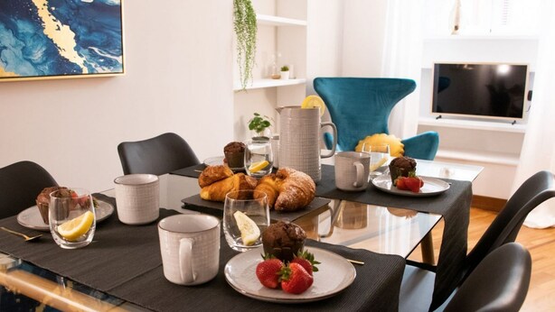 A dining area with a glass table set for breakfast, including croissants, strawberries, and coffee. - The Best Rent - Deluxe Piazza di Spagna Apartment (Roma)