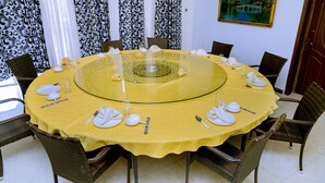Mesa redonda para seis personas con mantel amarillo, rodeada de sillas de mimbre.