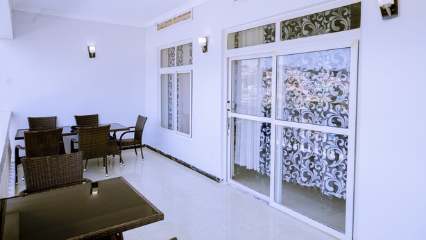 Un patio amplio con mesa y sillas, ventanas grandes con cortinas decorativas y un interior en tonos blancos.