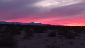 A mountain range silhouetted against a sunset sky. - Off grid camping, bring tents or camper van. The only frill is a clean outhouse! (Joshua Tree)