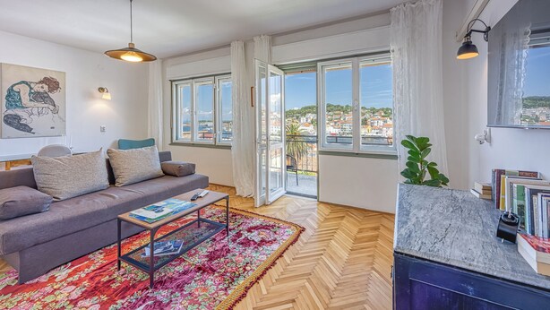 A modern living room with a sofa, coffee table, and a view of a cityscape through large windows.