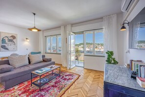 A living room with a sofa, coffee table, and a view of a cityscape through large windows.