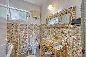 Een badkamer met patroon betegelde vloer, toilet, wastafel met spiegel en een raam.