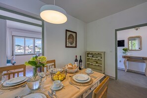 A dining area with a table set for four, a vase with flowers, a basket of bread, and a wine bottle.