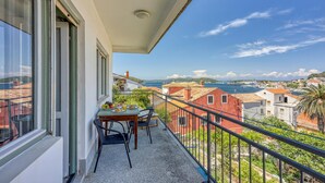 A balcony with a table and chairs, overlooking a coastal town with red buildings and a clear sky.