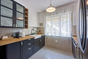 A modern kitchen with a wooden countertop, black cabinets, a white sink, and a stainless steel refrigerator.