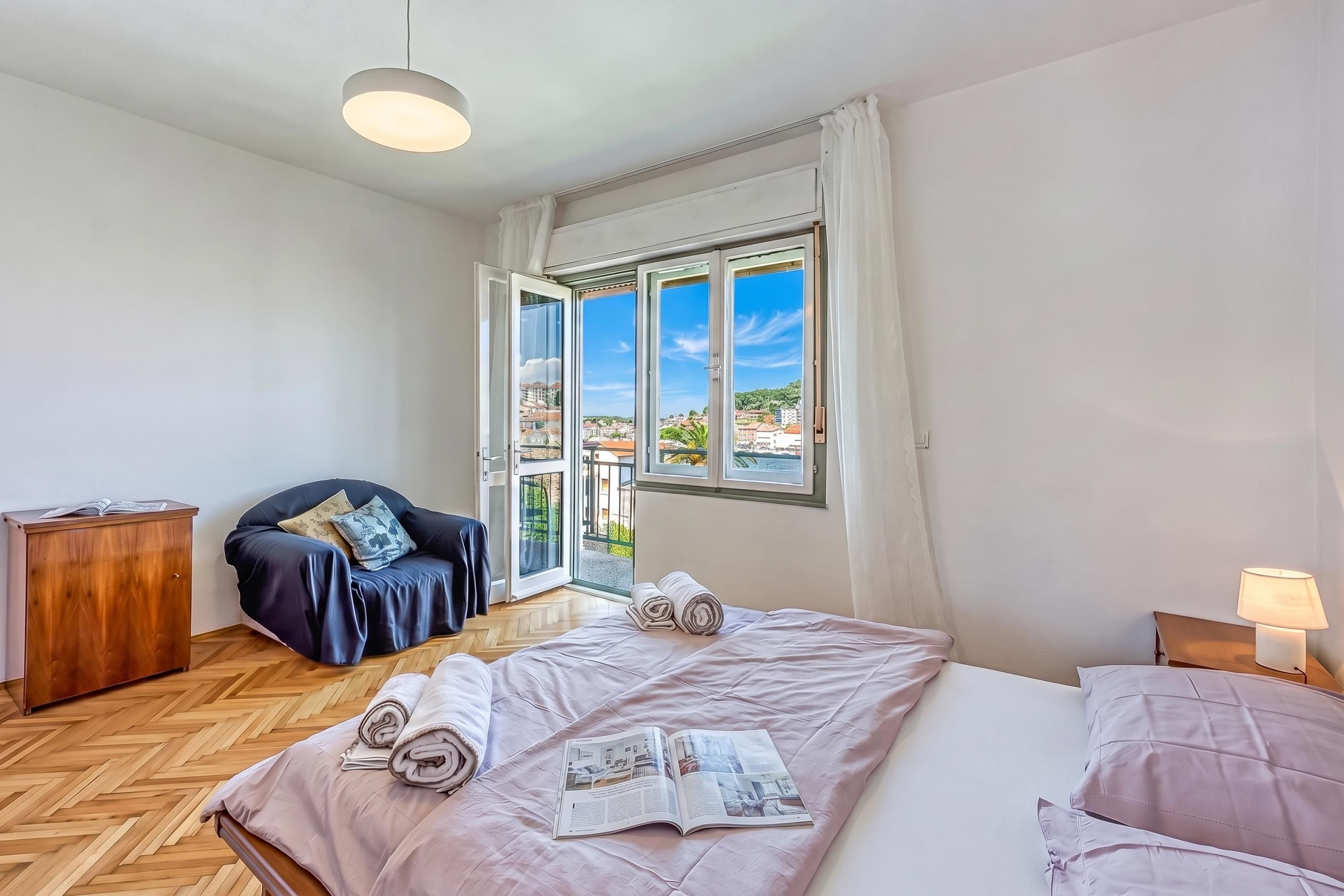 Een hotelkamer met een bed, een stoel, een bureau en uitzicht op de stad door grote ramen.