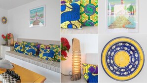 A room with a sofa adorned with colorful pillows, a framed picture on the wall, a decorative wooden light, and a patterned plate.