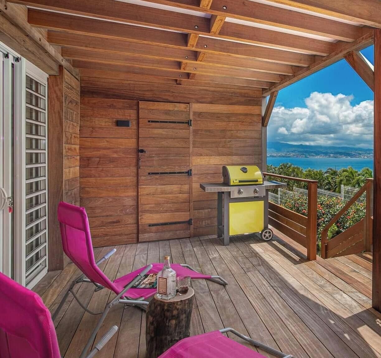 A wooden deck with a grill, chairs, and a view of the ocean.