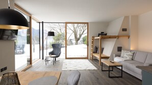 A modern living room with a sofa, a coffee table, and a chair. There is a large window providing a view of the outdoors. - Stadler Hof - Orangery (Lana)
