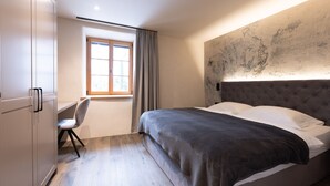 A modern bedroom with a large bed, a desk, and a chair. - Stadler Hof - Orangery (Lana)