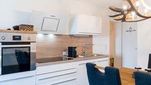 Een moderne keuken met witte kasten, een inbouwoven, een spoelbak en een eethoek met een houten tafel en blauwe stoelen.