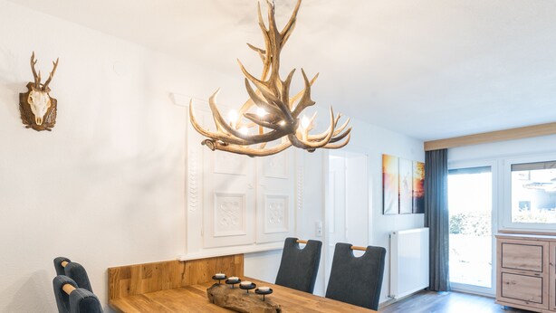 Een eetruimte met een houten tafel, zwarte bekleden stoelen en een kroonluchter versierd met gewei.