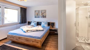 Een moderne slaapkamer met een houten bed, een nachtkastje, een raam met gordijnen en twee wanddecoraties.