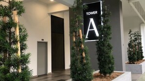 A modern building entrance with a sign reading "TOWER A" and a pathway lined with small trees.