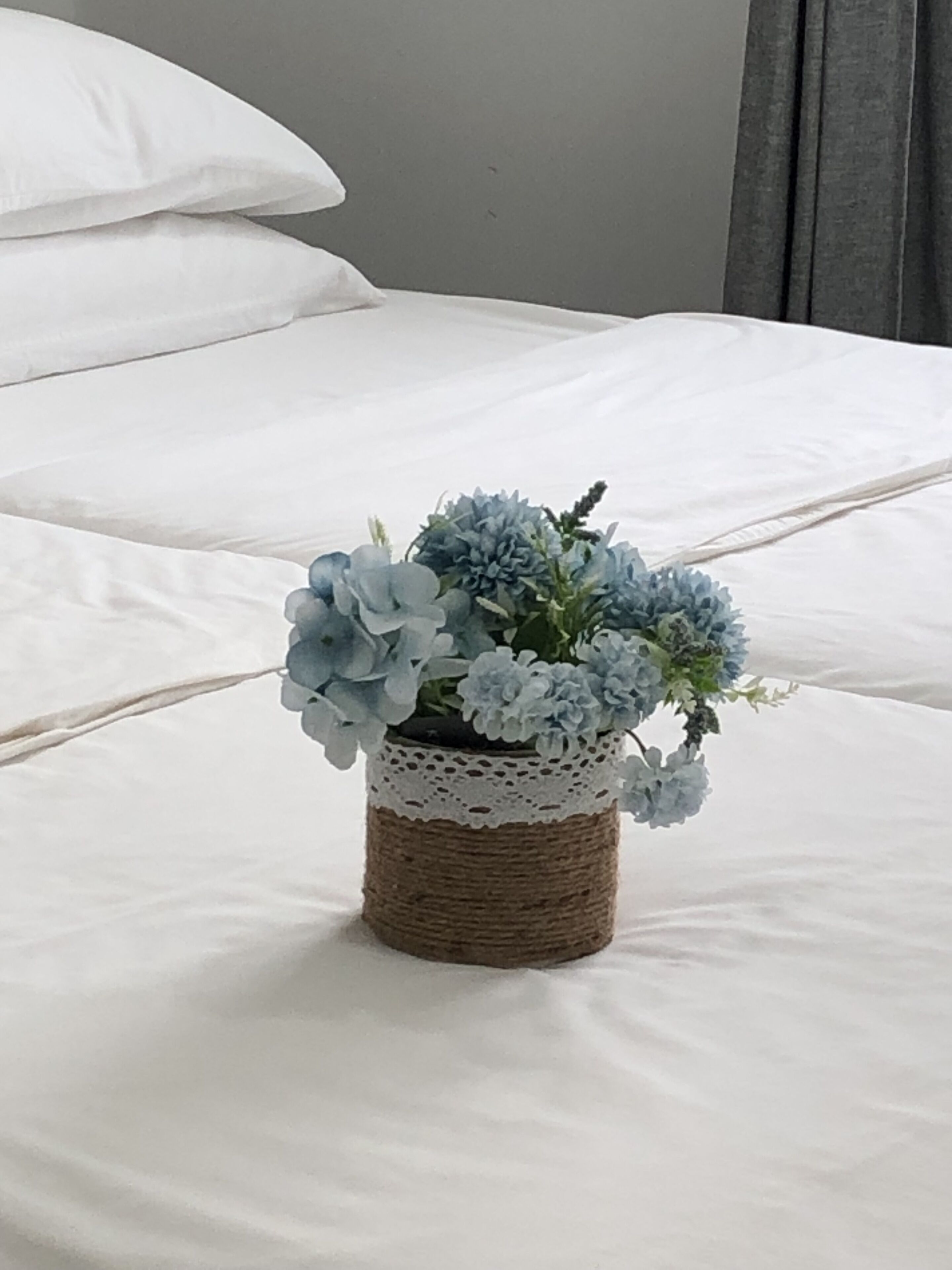 Un lit avec du linge de lit blanc et un panier tressé contenant des fleurs bleues.