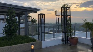 A rooftop terrace with a glass railing, potted plants, and street lamps.