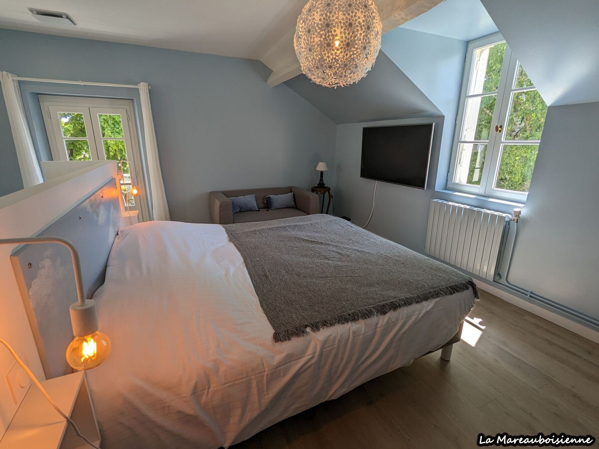 Un dormitorio con cama, televisión, ventana y candelabro.