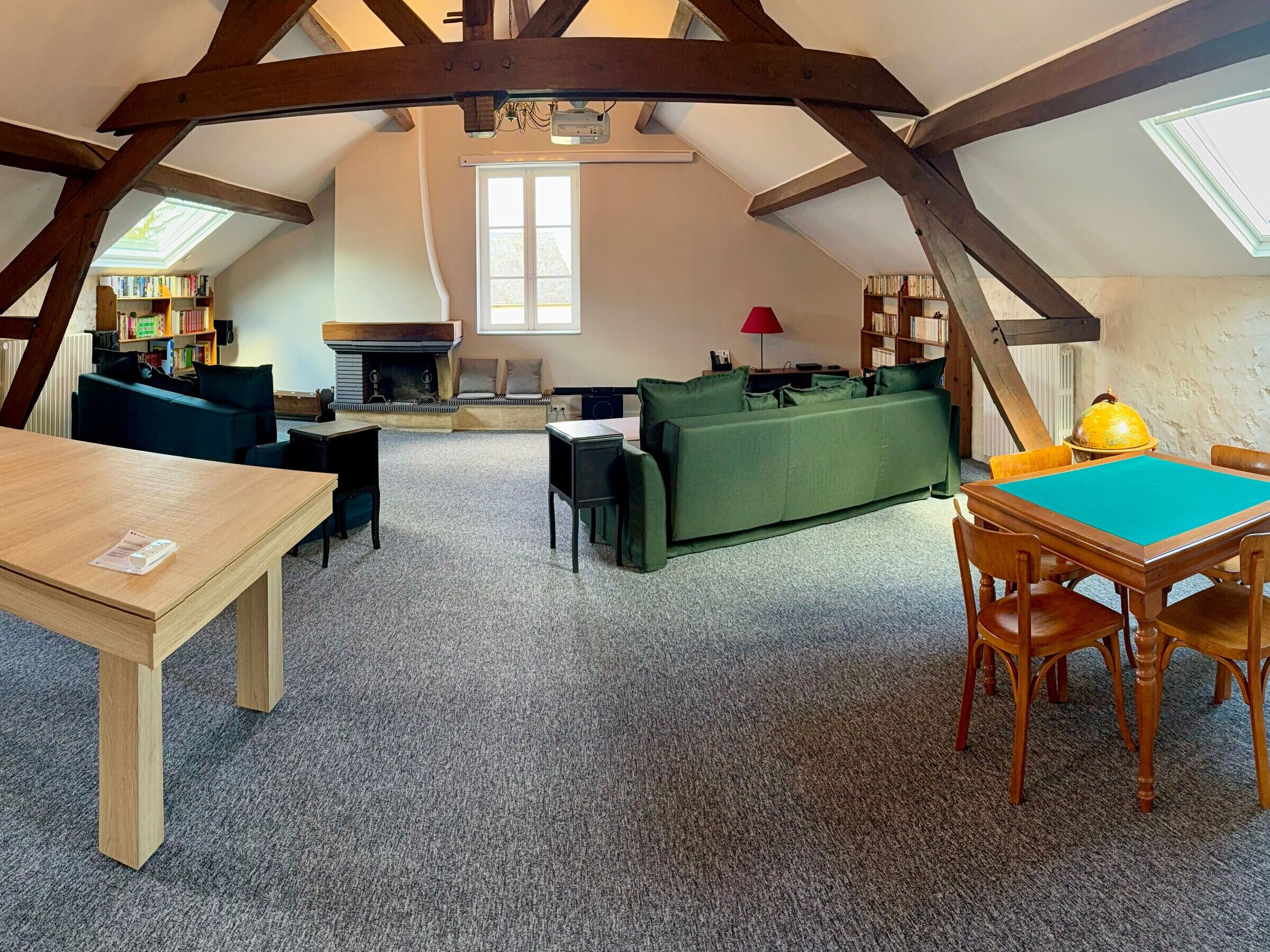 Ein Loft-Zimmer mit Holzbalkendecke, Kamin, einem grünen Sofa, einem Holztisch und einem Esstisch mit Stühlen.