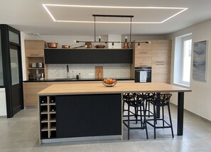 A modern kitchen with a central island, black cabinets, and a herringbone backsplash. - Charming Stone House with Park, Game Room, High-Speed WiFi, and Tennis Nearby (Mareau-aux-Bois)