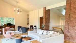 Una sala moderna con un sofá seccional blanco, un sillón rosa y un piano.