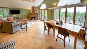 Un salón amplio con chimenea, comedor y ventanas grandes que ofrecen vistas al exterior.