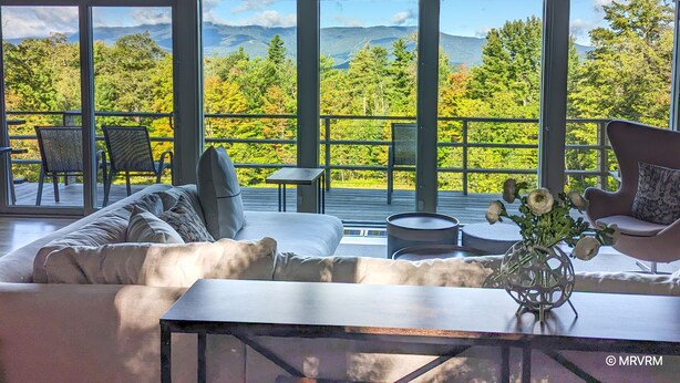Un salón moderno con un amplio ventanal que da a un paisaje montañoso y boscoso.