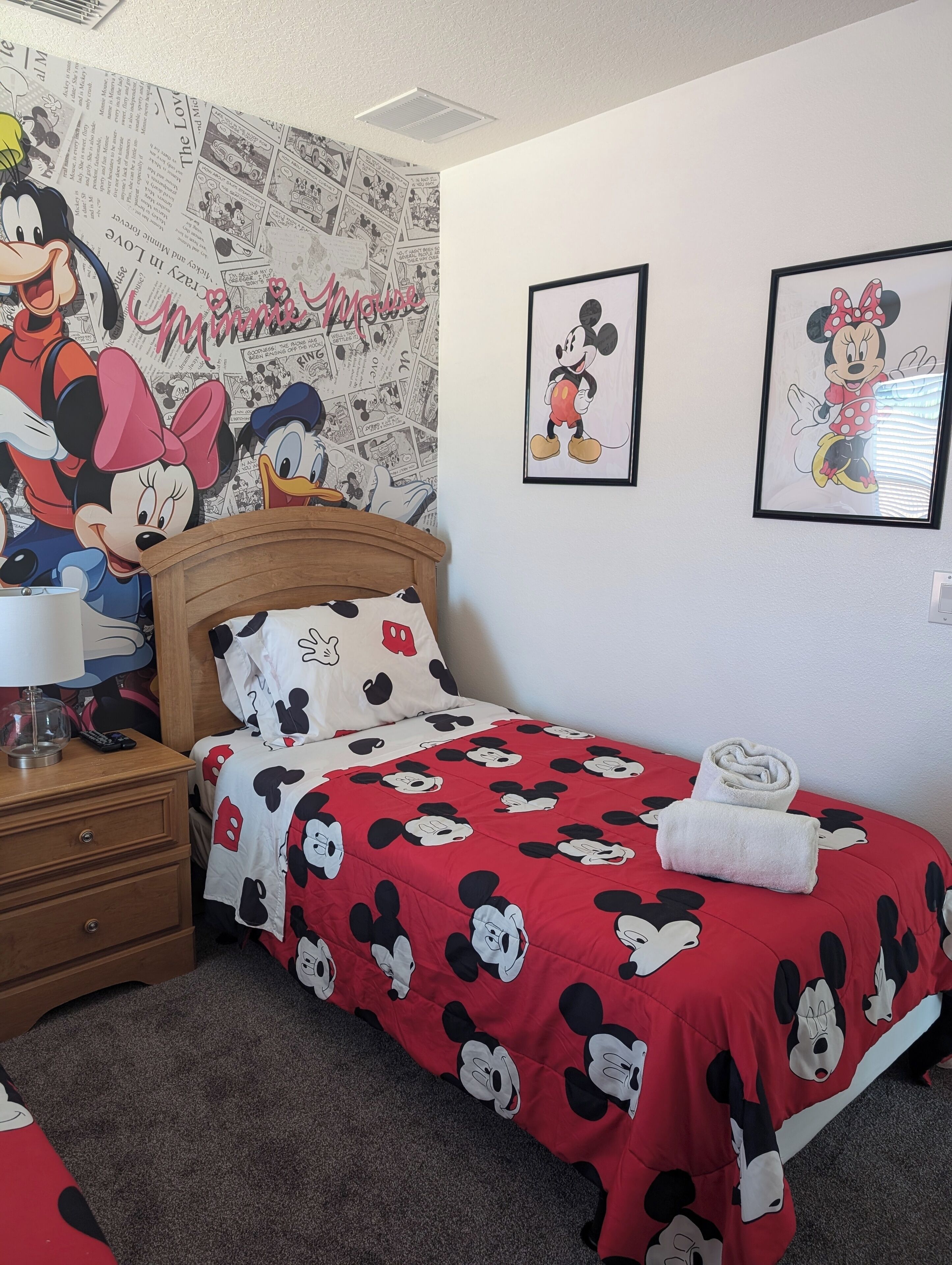 A hotel room with a Mickey Mouse themed bedspread, a headboard with Mickey and Minnie Mouse, and a wall with comic strip wallpaper.