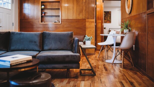 A modern living room with a dark leather sofa, wooden flooring, a small side table, and a dining area with white chairs and a table. - Escape to this artsy 2-bedroom MCM Guesthouse in charming Phoenix, OR. Unwind in the luxurious spa soaking tub after exploring Southern Oregon. Features high-end design for a stylish, quiet retreat. (Phoenix)