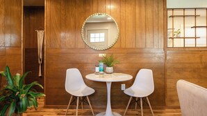 A room with wooden panel walls, a round mirror with a gold frame, two white chairs around a small white table, and a potted plant. - Escape to this artsy 2-bedroom MCM Guesthouse in charming Phoenix, OR. Unwind in the luxurious spa soaking tub after exploring Southern Oregon. Features high-end design for a stylish, quiet retreat. (Phoenix)