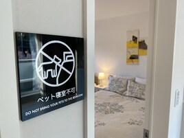 Placa proibindo animais de estimação no quarto, cama com roupa de cama florida e mesa de cabeceira com abajur.