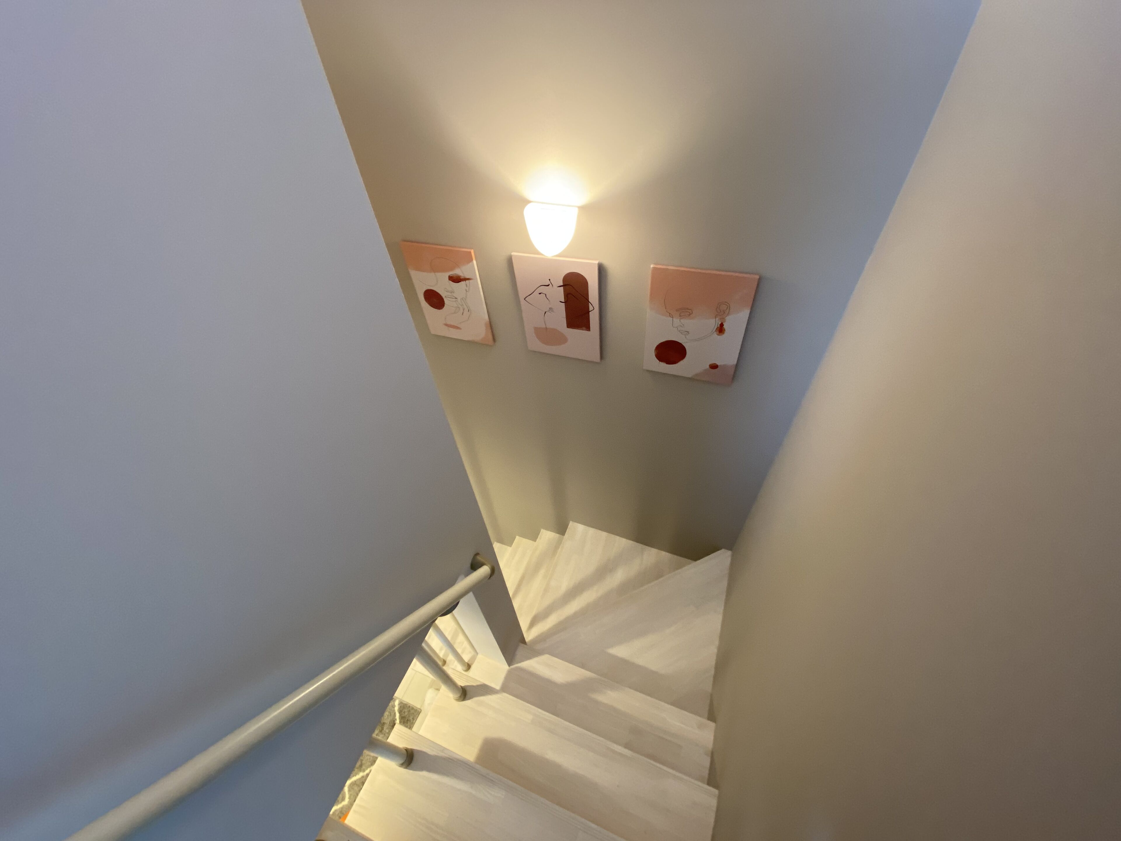 A staircase with a handrail, light fixture, and three wall-mounted artworks.