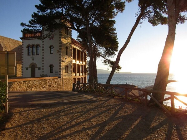 A coastal building with a stone facade, a balcony, and a view of the sea.