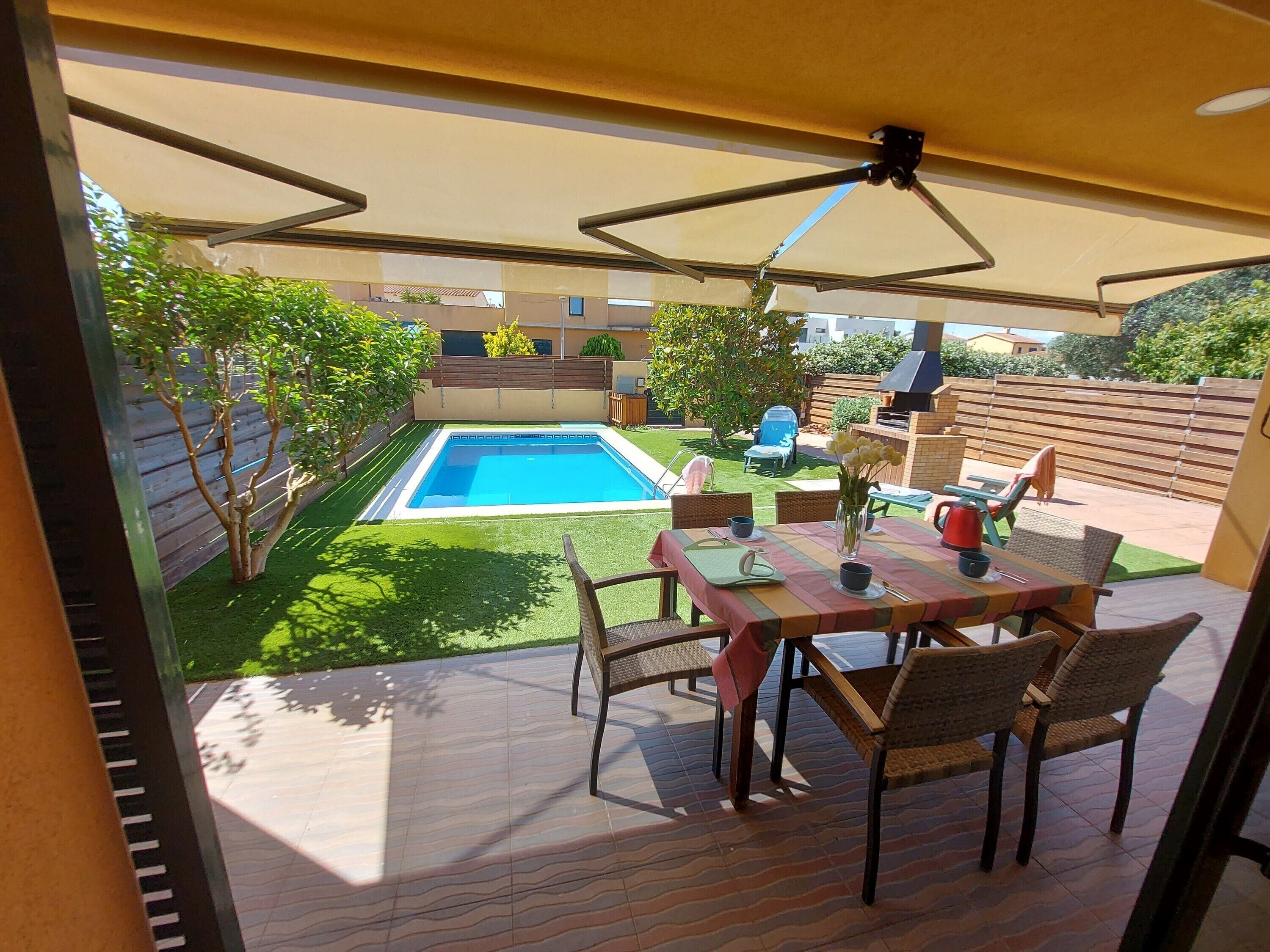 Een terras met een zwembad, tuinmeubilair en een barbecue.