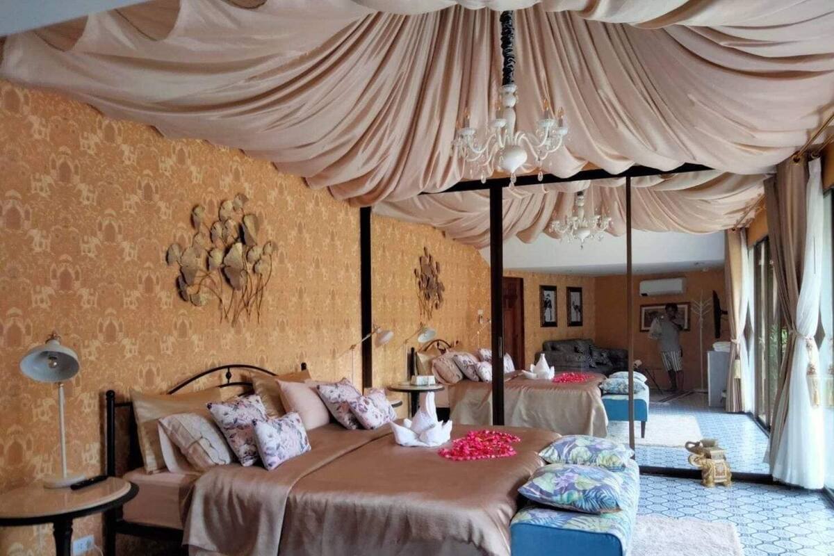 A bedroom with a large bed, a bedside table, a chair, a small table, and a chandelier.