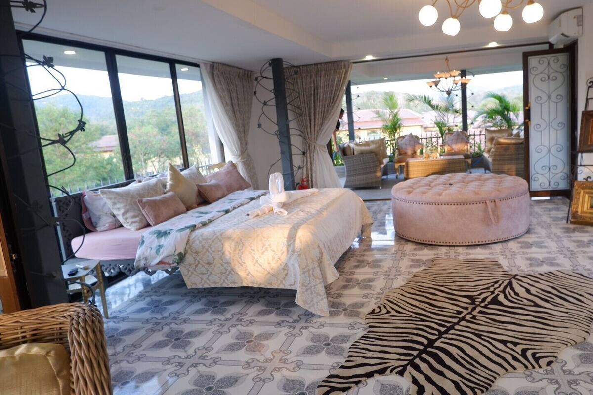 A spacious bedroom with a large bed, a round ottoman, and a zebra-patterned rug.