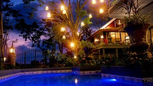 Zona de piscina con fuente, rodeada de vegetación exuberante e iluminación decorativa.