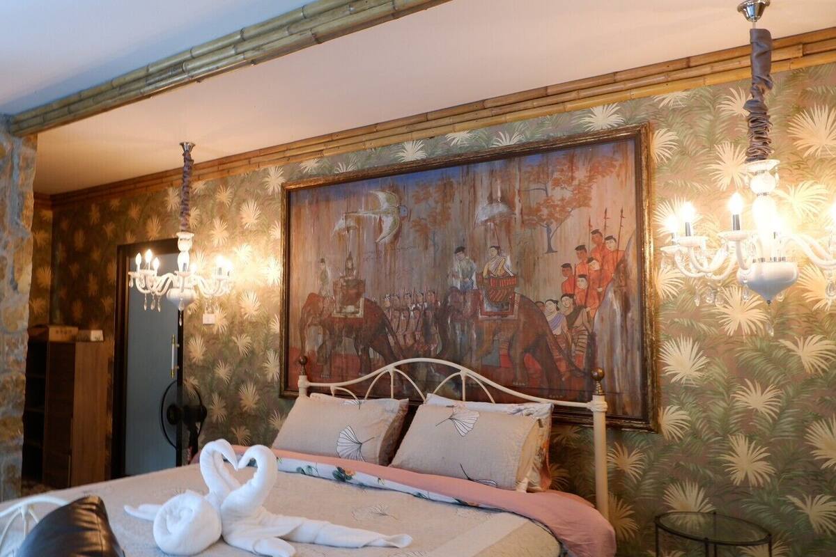 A hotel room with a bed, a clock, a chandelier, and a large painting on the wall.