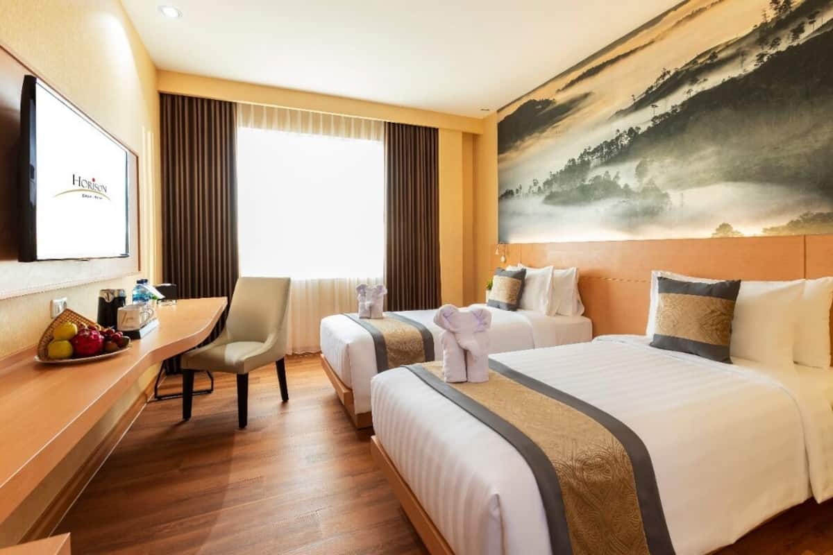 Een hotelkamer met twee bedden, een bureau, een stoel en een groot schilderij aan de muur.