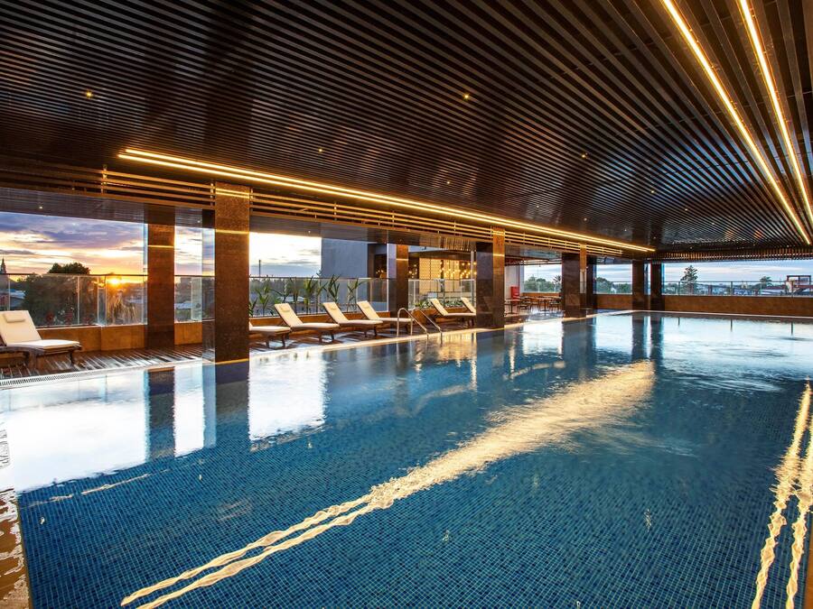 An indoor swimming pool with lounge chairs and a sunset view through large windows.