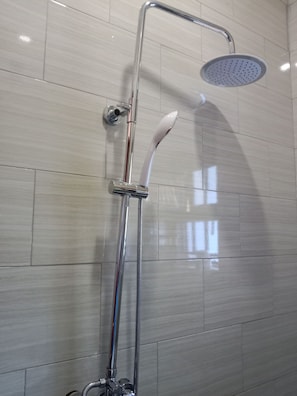 Une douche moderne dotée d’un pommeau de douche à main et d’un grand pommeau de douche suspendu imitant une pluie fine.