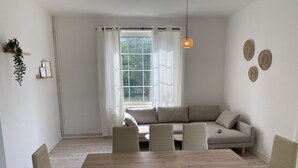Una sala de estar moderna con una mesa de comedor de madera, sofás beige y un amplio ventanal con cortinas blancas.