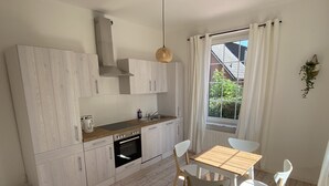 Una cocina moderna con armarios blancos, horno empotrado y comedor con mesa y sillas de madera.