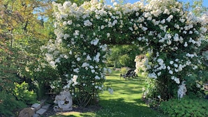 Ein Garten mit einem weißen, blumengeschmückten Bogen, einer Statue und einer Sitzgelegenheit.