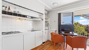 A modern kitchen with white cabinets, a gas stove, and a dining area with two orange chairs. - Fremantle's Best | Urban Studio (Fremantle)
