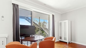 A modern living room with a large window, a dining table with chairs, a white cabinet, and a staircase leading outside. - Fremantle's Best | Urban Studio (Fremantle)