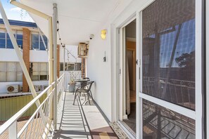 Ein Balkon mit Tisch und Stühlen, einem Blumentopf und Blick auf ein Gebäude mit großen Fenstern.