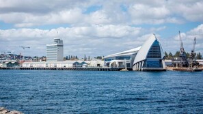 Ein Gebäude am Wasser mit modernem Design, das ein markantes, gewölbtes Dach und einen hohen Turm zeigt.