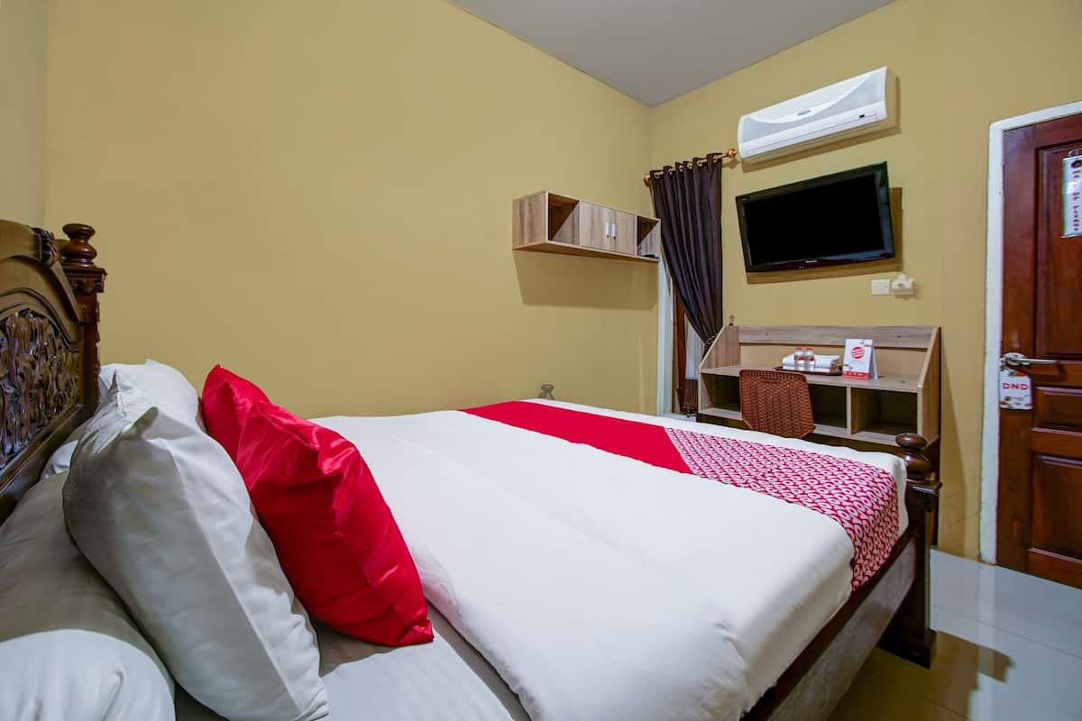 A hotel room with a bed, a TV mounted on the wall, a desk with a chair, and a door with a sign.